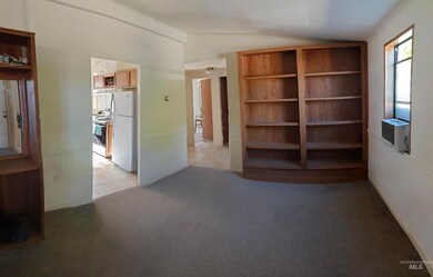 Unfurnished bedroom with vaulted ceiling, freestanding refrigerator, and light colored carpet