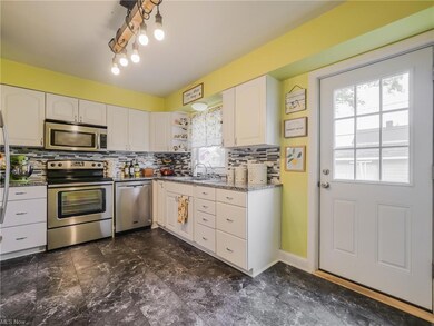 Kitchen featuring tasteful backsplash, an inviting chandelier, stainless steel appliances, and dark tile flooring