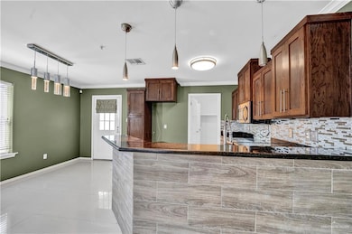 Kitchen featuring a peninsula, stainless steel microwave, visible vents, backsplash, and crown molding