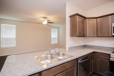 Kitchen featuring stainless steel dishwasher, a sink, light countertops, ceiling fan, and dark wood-style floors