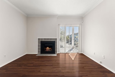 Unfurnished living room featuring dark wood finished floors, a textured ceiling, crown molding, and a tile fireplace