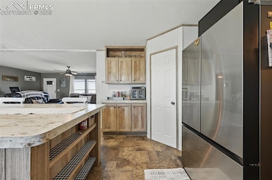 Kitchen with freestanding refrigerator, dark stone finish floors, light countertops, open floor plan, and a ceiling fan