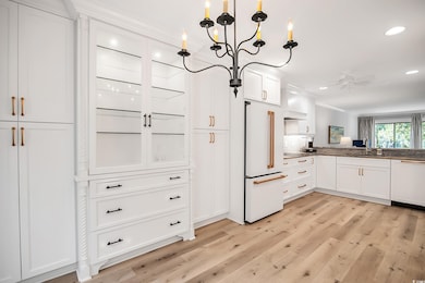Kitchen featuring white cabinets, high end white fridge, paneled dishwasher, light wood finished floors, and ornamental molding