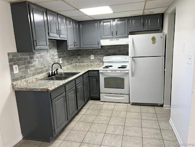 Kitchen featuring gray cabinetry, white appliances, tasteful backsplash, a drop ceiling, and light tile patterned floors