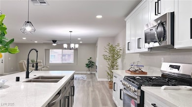 Kitchen with appliances with stainless steel finishes, white cabinets, light stone countertops, light wood finished floors, and recessed lighting