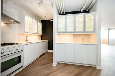 Kitchen with oven, gas cooktop, wall chimney exhaust hood, light wood-style flooring, and a stainless sink