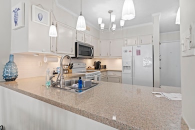 Kitchen featuring white appliances, white cabinets, tasteful backsplash, crown molding, and pendant lighting