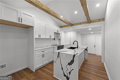 Kitchen with a sink, range with electric cooktop, white cabinets, a kitchen island with sink, and dark wood-type flooring