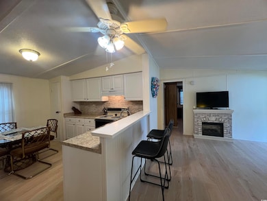 Kitchen featuring vaulted ceiling, light wood-type flooring, backsplash, white cabinetry, and ceiling fan