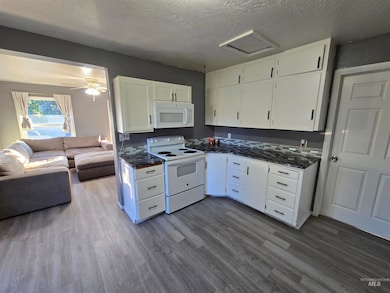 Kitchen featuring open floor plan, white appliances, white cabinets, dark wood-type flooring, and a textured ceiling