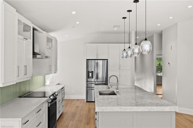 Kitchen with appliances with stainless steel finishes, vaulted ceiling, a center island with sink, light wood finished floors, and white cabinetry