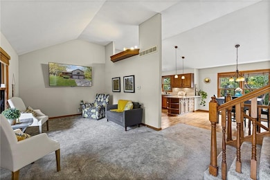 Living area with light colored carpet, stairway, high vaulted ceiling, and a chandelier