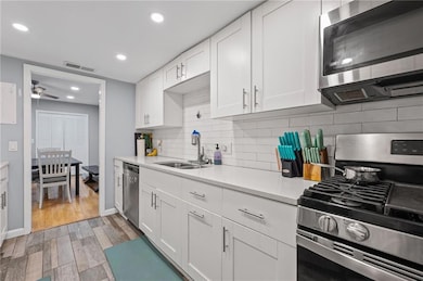 Kitchen with appliances with stainless steel finishes, a sink, light countertops, white cabinetry, and recessed lighting
