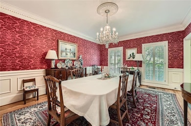 Dining area featuring a chandelier, a wainscoted wall, wallpapered walls, wood finished floors, and crown molding