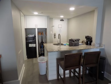 Kitchen with light stone counters, a peninsula, white cabinetry, wood finished floors, and a breakfast bar