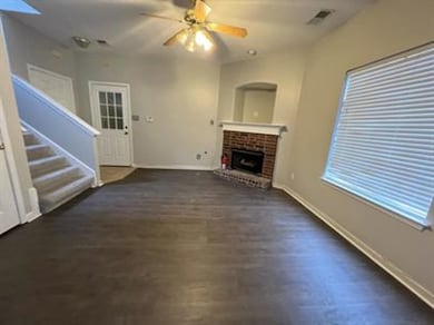 Unfurnished living room with a brick fireplace, a ceiling fan, stairway, and wood finished floors