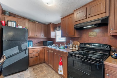 Kitchen featuring black appliances, light countertops, under cabinet range hood, vaulted ceiling, and brown cabinets