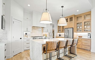 Kitchen featuring a kitchen bar, light stone counters, a center island with sink, backsplash, and stainless steel appliances
