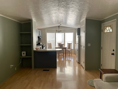 Living room with ornamental molding, a chandelier, a textured ceiling, vaulted ceiling, and light wood-style flooring