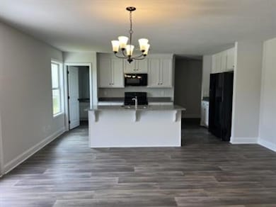 Kitchen featuring a breakfast bar, black appliances, a chandelier, a center island with sink, and decorative light fixtures