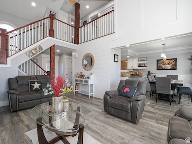 Living room with a high ceiling, a decorative wall, wood finished floors, recessed lighting, and ornamental molding