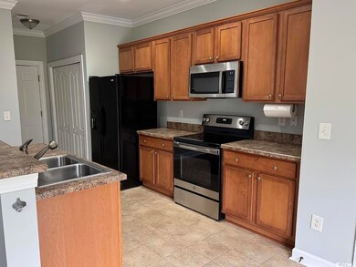 Kitchen featuring appliances with stainless steel finishes, brown cabinetry, crown molding, and dark countertops