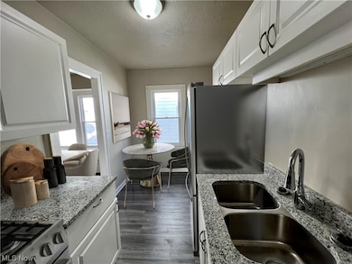Kitchen featuring light stone countertops, stove, a textured ceiling, white cabinetry, and dark hardwood / wood-style floors