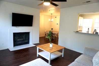 Living room featuring ceiling fan, wood finished floors, a brick fireplace, and a chandelier