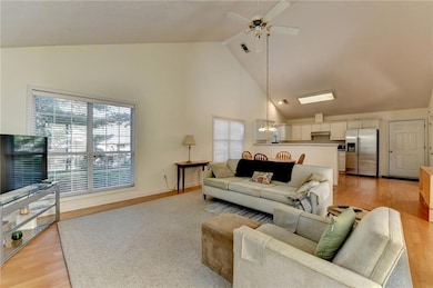 Living area featuring plenty of natural light, high vaulted ceiling, a ceiling fan, and light wood-style flooring