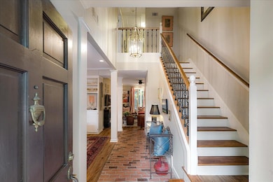 Entrance foyer featuring brick floors, ornate columns, stairway, a towering ceiling, and a chandelier
