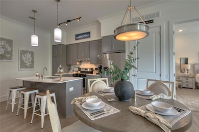 Kitchen featuring stainless steel electric stove, a center island with sink, sink, gray cabinets, and ornamental molding
