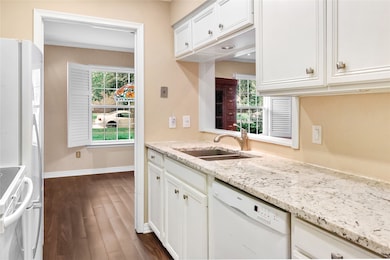 Kitchen with white appliances, dark wood-style flooring, white cabinetry, and light stone counters