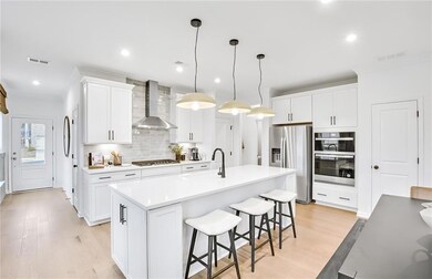 Kitchen with wall chimney range hood, stainless steel appliances, light wood-style floors, tasteful backsplash, and a breakfast bar area