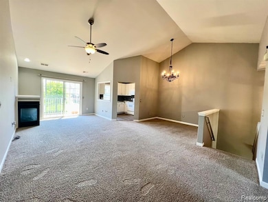 Unfurnished living room with a chandelier, light carpet, a fireplace, a ceiling fan, and high vaulted ceiling