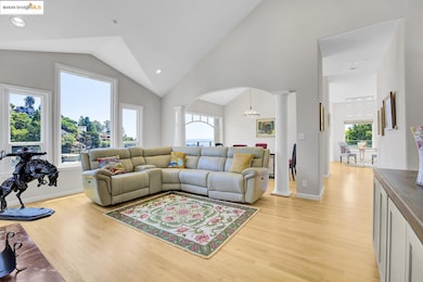 Living room with decorative columns, light wood-type flooring, arched walkways, lofted ceiling, and a chandelier