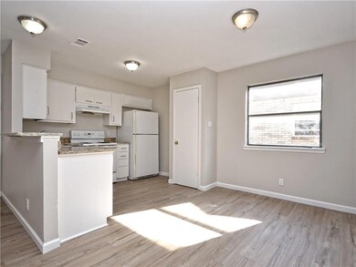 Kitchen with white appliances, under cabinet range hood, light wood finished floors, light countertops, and white cabinets