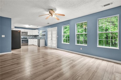 Unfurnished living room featuring a ceiling fan, light wood-style floors, and a textured ceiling