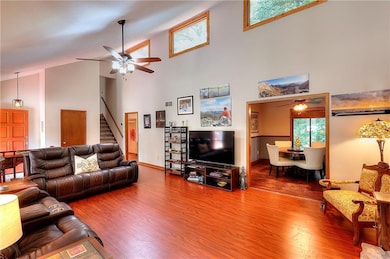 Living area with ceiling fan, high vaulted ceiling, wood finished floors, and stairway