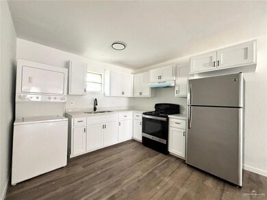 Kitchen featuring white cabinets, stainless steel fridge, black electric range oven, and stacked washing maching and dryer