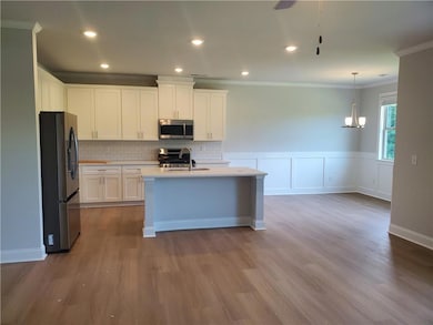 Kitchen featuring appliances with stainless steel finishes, white cabinetry, crown molding, dark wood-style flooring, and a center island with sink
