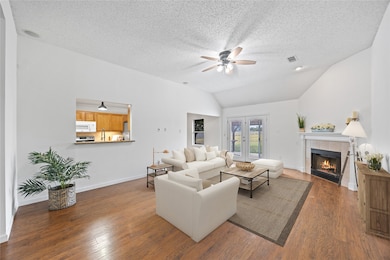 Living area with dark wood finished floors, vaulted ceiling, a tile fireplace, a ceiling fan, and a textured ceiling