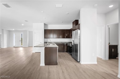 Kitchen featuring dark brown cabinets, recessed lighting, an island with sink, light stone countertops, and appliances with stainless steel finishes