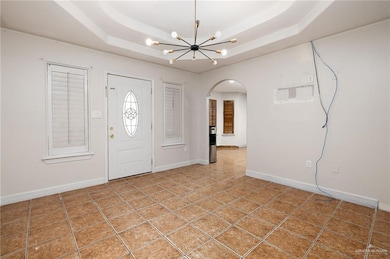 Tiled foyer entrance with a notable chandelier, a raised ceiling, arched walkways, and baseboards