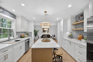 Kitchen with backsplash, light wood-type flooring, appliances with stainless steel finishes, white cabinetry, and recessed lighting