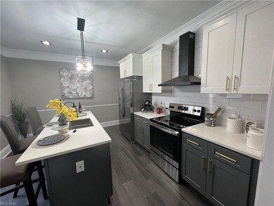 Kitchen featuring decorative light fixtures, tasteful backsplash, dark hardwood flooring, wall chimney range hood, and white cabinetry