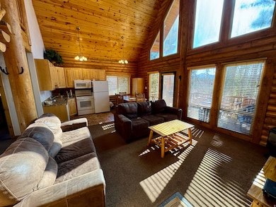 Living room featuring high vaulted ceiling, rustic walls, a chandelier, wood ceiling, and dark colored carpet