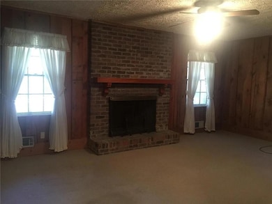 Unfurnished living room with wood walls, a brick fireplace, a textured ceiling, carpet flooring, and a ceiling fan