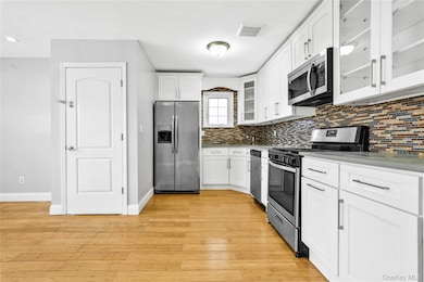 Kitchen featuring backsplash, white cabinetry, appliances with stainless steel finishes, light wood-style flooring, and visible vents