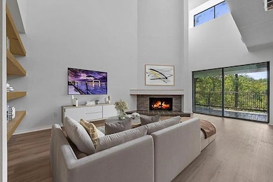 Living room with a warm lit fireplace, wood finished floors, and a towering ceiling