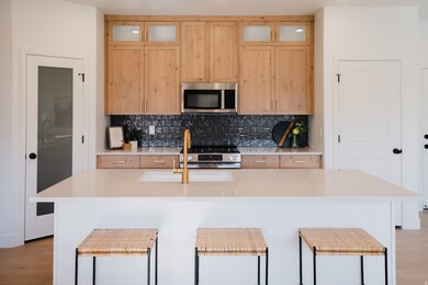 Kitchen featuring light wood finished floors, light brown cabinets, stainless steel appliances, and decorative backsplash